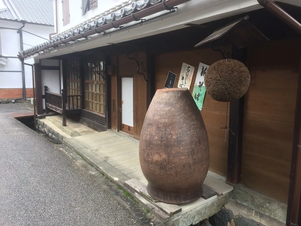 Old sake brewery front with a large clay jar and a cedar ball hanging by the door